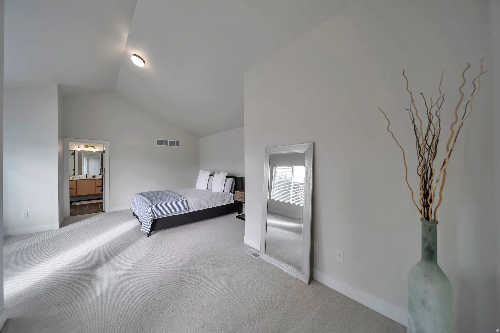 Spacious room featuring vaulted ceilings, light-toned carpeting, and a doorway revealing a bathroom with a dual vanity