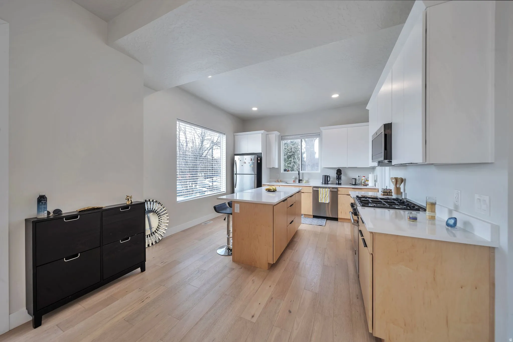 Open-concept kitchen featuring light wood-finish flooring, white cabinetry, a central island with bar seating, a gas range, and stainless steel appliances