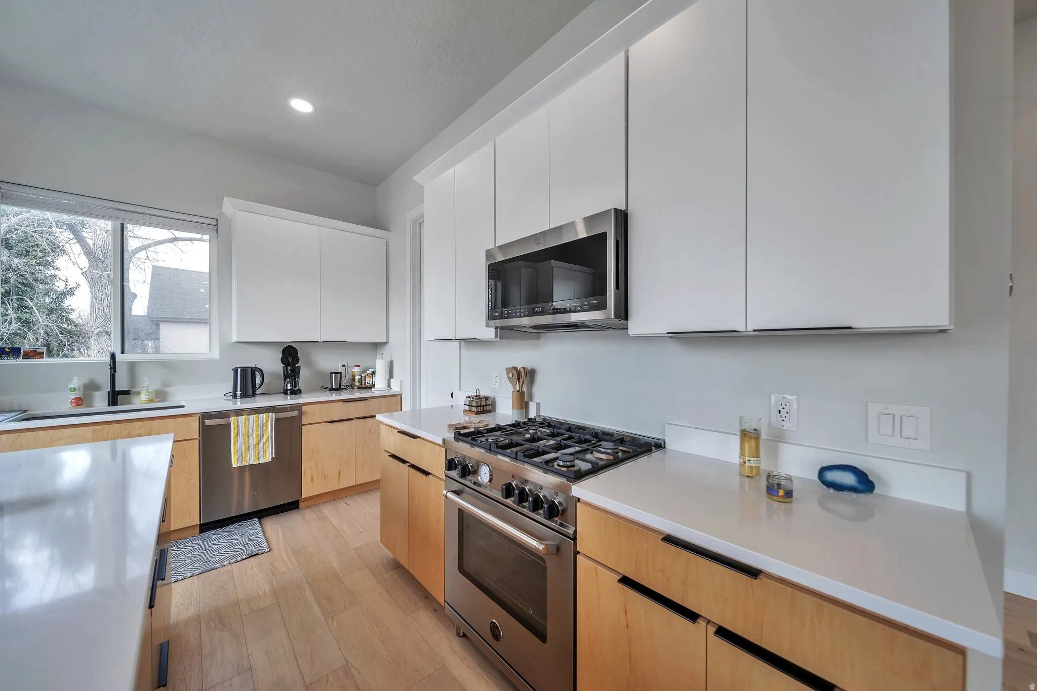Modern kitchen featuring light wood-finish lower cabinetry, white upper cabinetry, and light-toned countertops