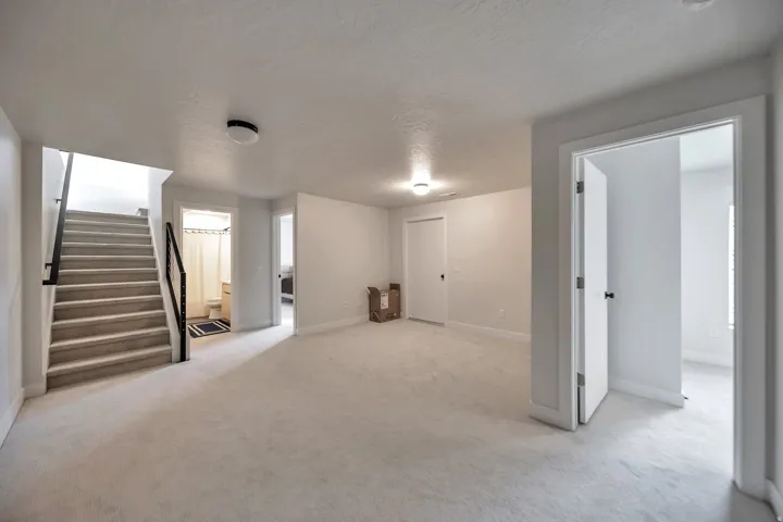 Carpeted open area featuring a staircase with black metal railings, white walls, and flush-mount lighting