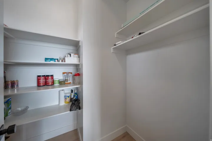 Walk-in pantry featuring white shelving, light wood-finish flooring, and white baseboards