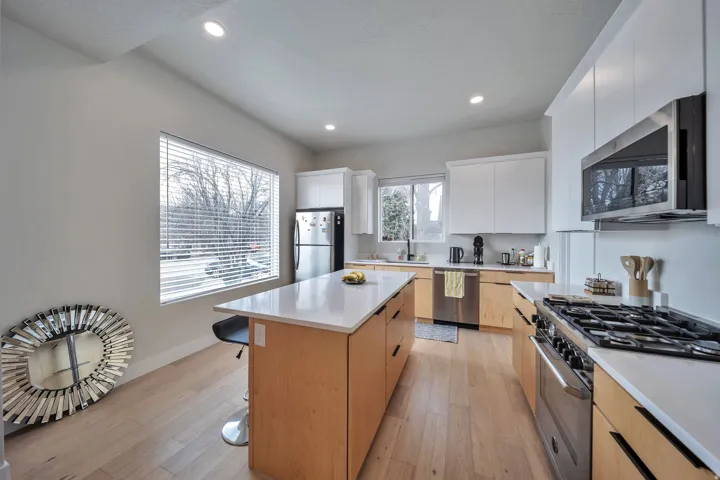 Contemporary kitchen featuring light wood-finish flooring, white flat-panel cabinetry, a light-toned island with integrated storage, and stainless steel appliances