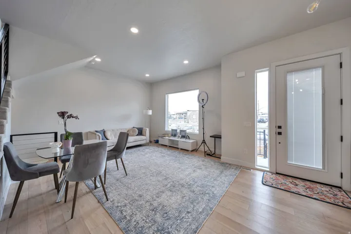 Bright open-concept living area featuring light wood-finish flooring, recessed lighting, and a large front window with blinds