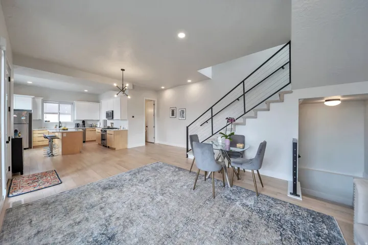 Open-concept living area featuring light wood-finish flooring, a modern black metal and cable staircase railing, recessed lighting, white perimeter cabinetry, and an island with light wood-finish base cabinets