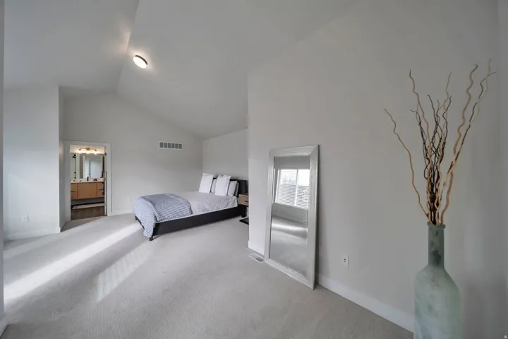 Spacious room featuring vaulted ceilings, light-toned carpeting, and a doorway revealing a bathroom with a dual vanity