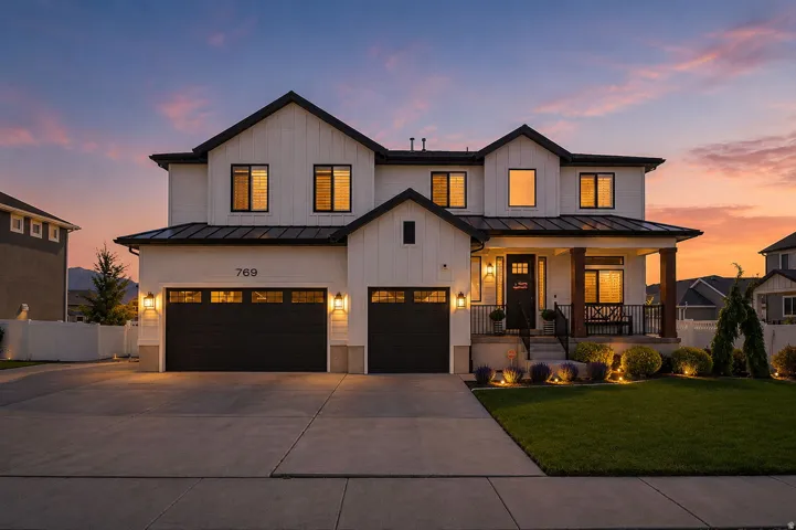 https://www.utahrealestate.com/lip/photo/listno/2157503#Modern farmhouse exterior featuring white board and batten siding, black trim windows, a covered front porch with wood columns, a two-car garage with black doors, and a manicured front lawn with land