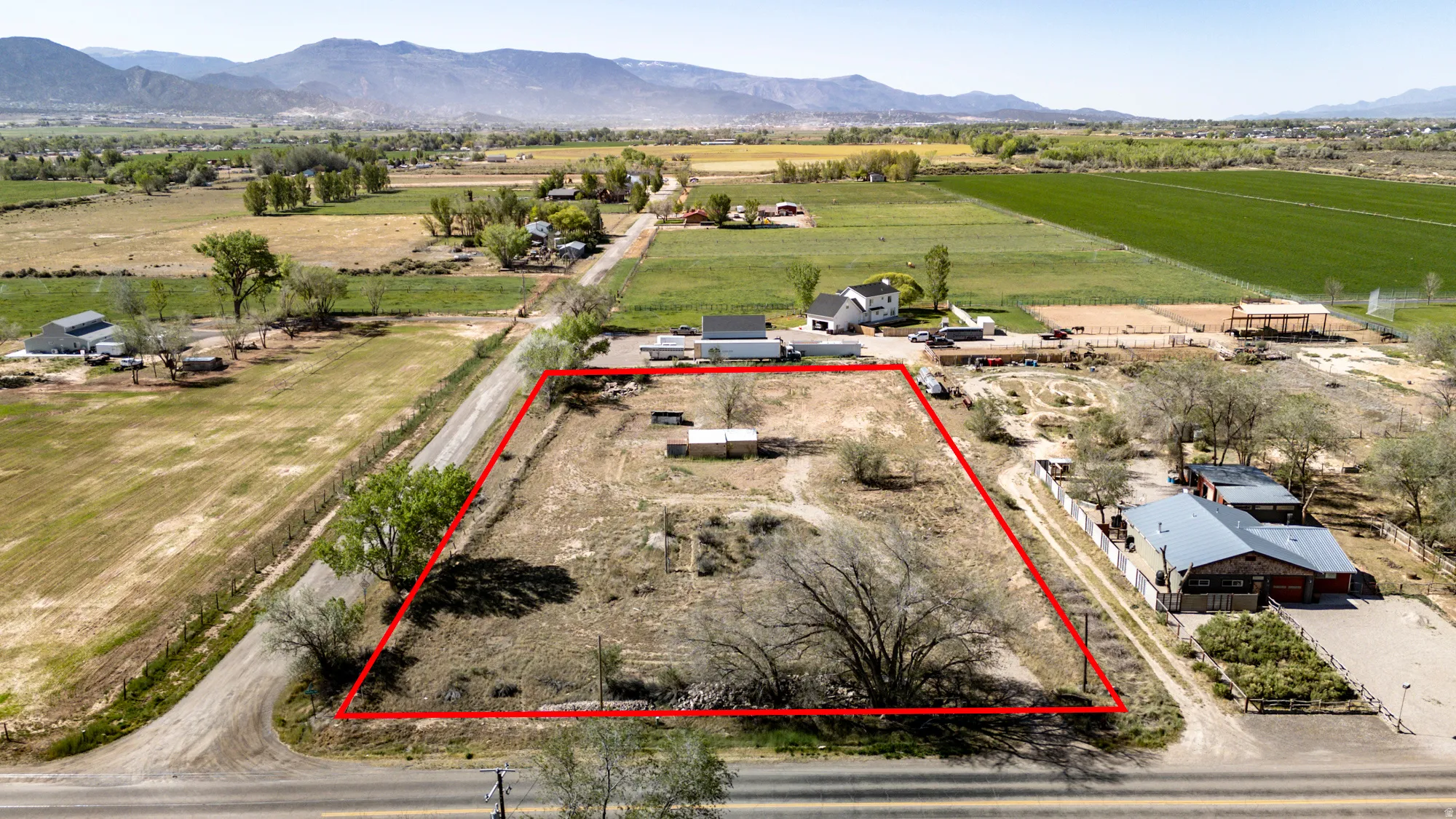 Expansive vacant lot featuring an irregular shape and mature trees, bordered by a paved road