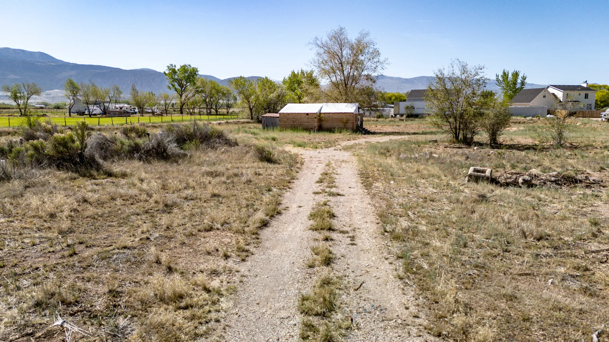 Expansive rural land featuring a gravel driveway and a brick outbuilding with a metal roof