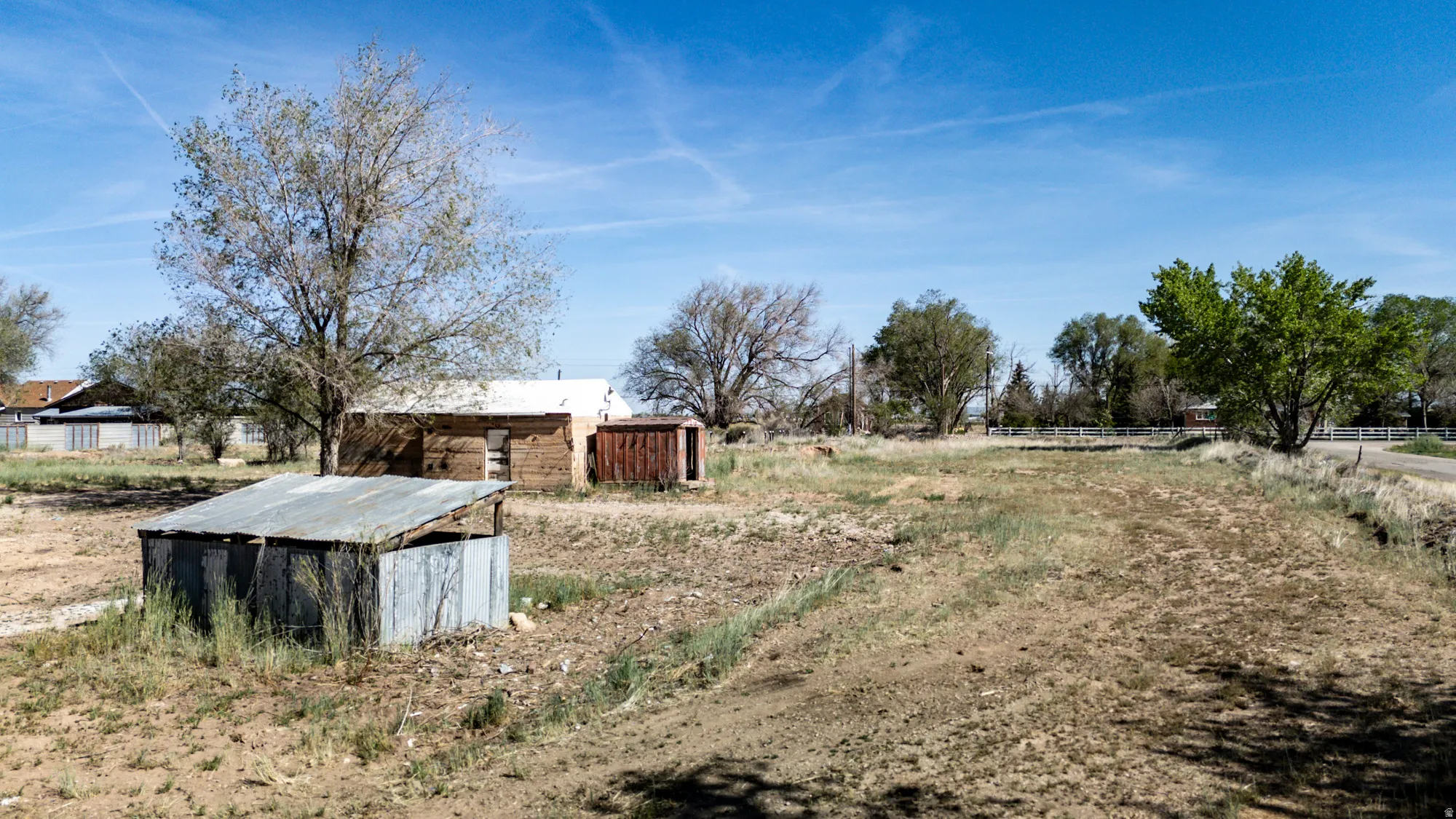 Expansive open land featuring a detached shed with a metal roof and a wood-sided structure with a white roof