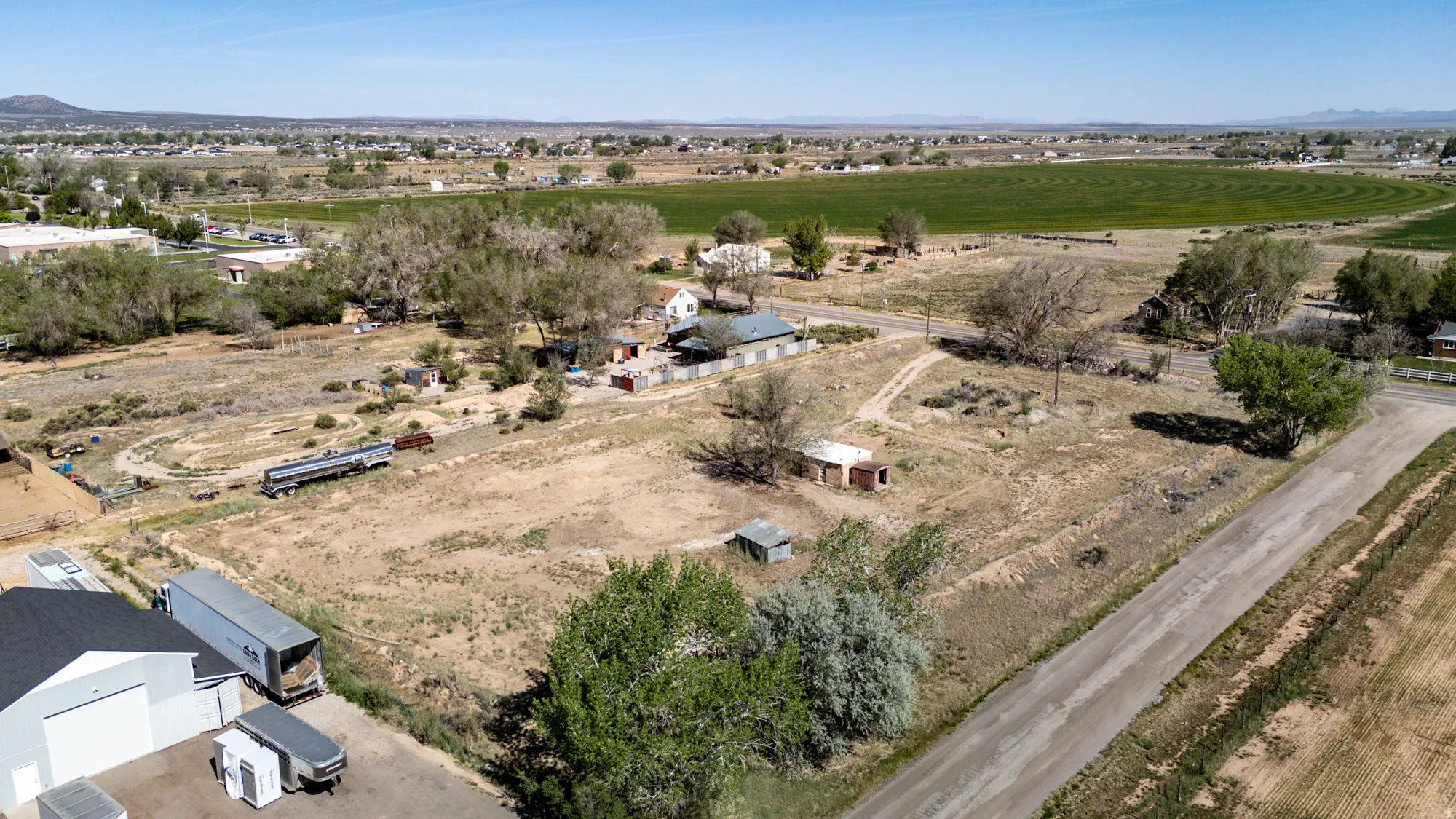 Expansive rural property featuring an unpaved road, mature trees, and a distant field