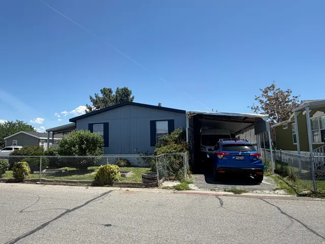 Light blue exterior siding with dark blue window shutters, a covered carport, and mature landscaping