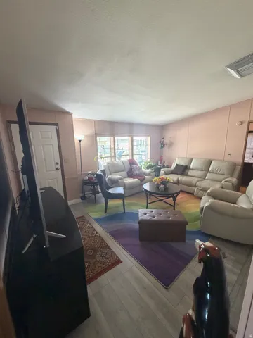 Spacious living area featuring wood-finish flooring, a white paneled door, and multiple windows