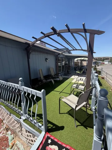 Outdoor patio featuring an attached pergola, artificial turf flooring, and decorative railing