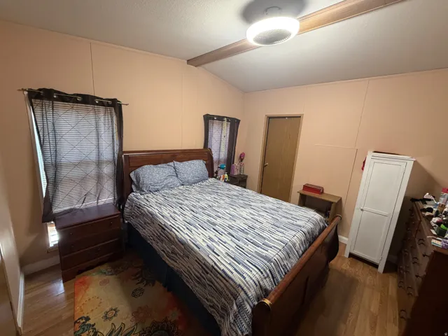 Bedroom featuring light wood-finish flooring, two windows with blinds, a ceiling-mounted light fixture, and a solid wood interior door
