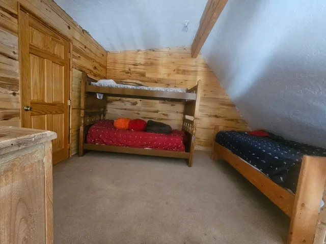 Wood-paneled room featuring an exposed beam, sloped ceiling, and wood-finish door