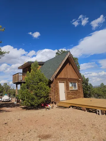 Log cabin exterior featuring a green shingle roof, a second-story balcony, a prominent front deck, and natural wood siding