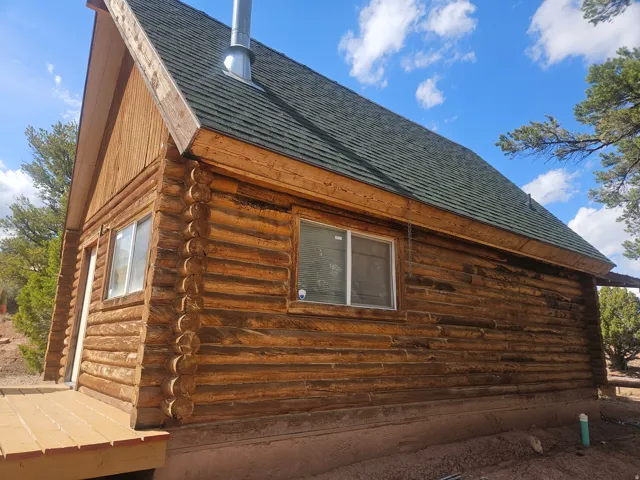Log cabin exterior featuring a dark green shingle roof, exposed timber siding, and white-framed windows