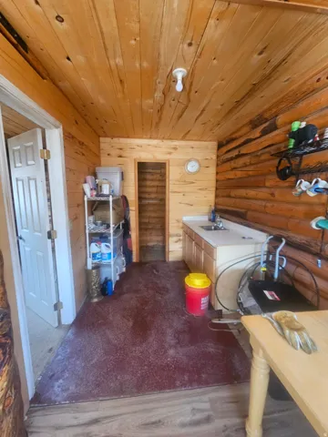 Room featuring natural wood plank walls and ceiling, a built-in sink with a light-toned cabinet, and mixed flooring with wood-finish planks and a red-toned area