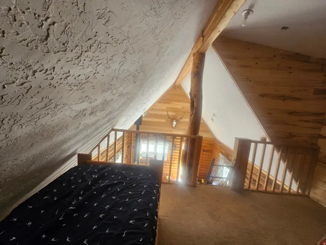 Loft area featuring exposed wood beams, wood-finish paneling, textured vaulted ceiling, and wood railings overlooking the level below