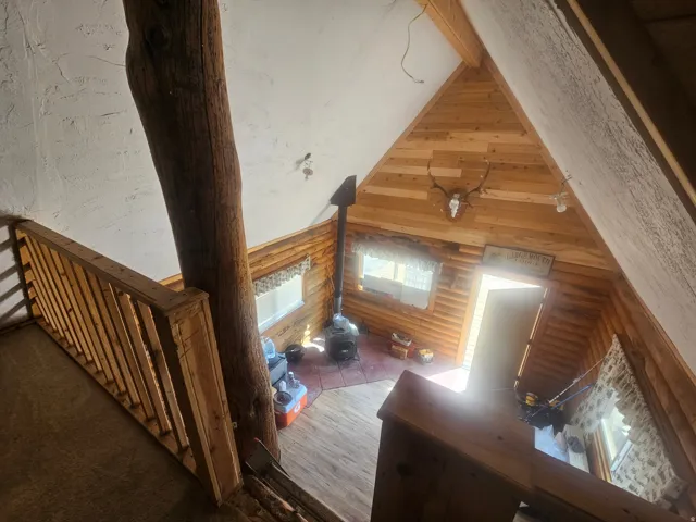 Vaulted ceiling with wood paneling, wood-finish flooring, and a wood-burning stove with a metal chimney