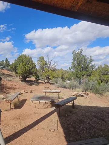 Outdoor entertainment space featuring a stone-clad fire pit with a metal grate, surrounded by three rustic wooden benches
