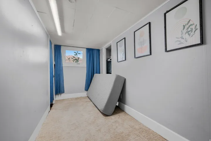 Light gray interior walls with white trim, beige carpeting, and a single window with blue drapes