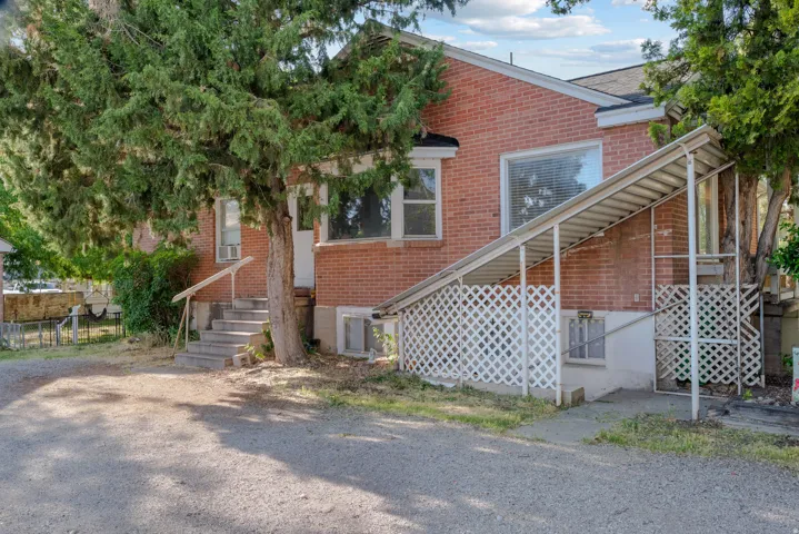 Brick exterior with a mature tree, concrete steps with handrail, and a covered side entrance featuring lattice screening