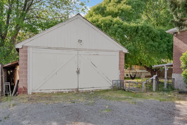 Detached garage structure with white siding and double barn doors, complemented by a brick base