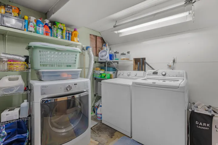 Dedicated laundry area featuring a front-load dryer, top-load washing machine, and wall-mounted shelving