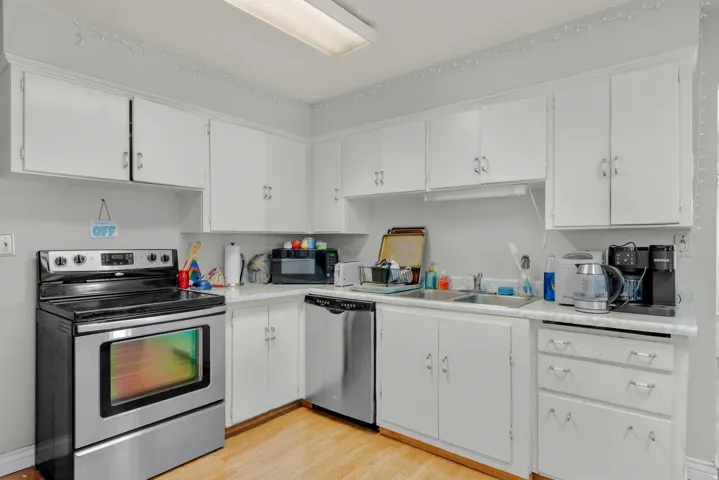 Kitchen featuring white cabinetry with silver hardware, white countertops, stainless steel range, and wood-finish flooring