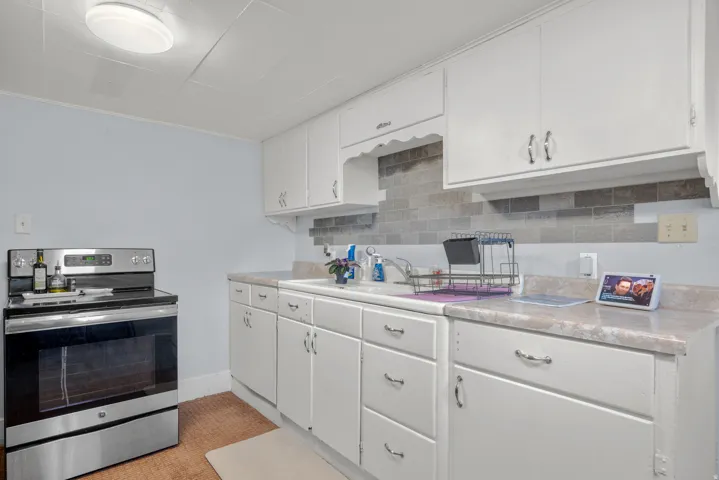Kitchen featuring white cabinetry with curved hardware, a stainless steel range, and a tiled backsplash