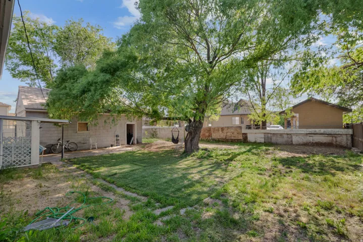 Expansive yard featuring mature trees, a detached block structure, and a covered patio area