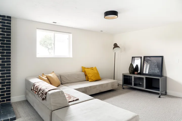 Carpeted living space featuring a window, white walls, and a black brick-clad column