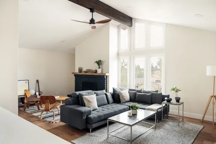 Vaulted ceiling living room featuring a dark wood beam, modern ceiling fan, and large picture windows