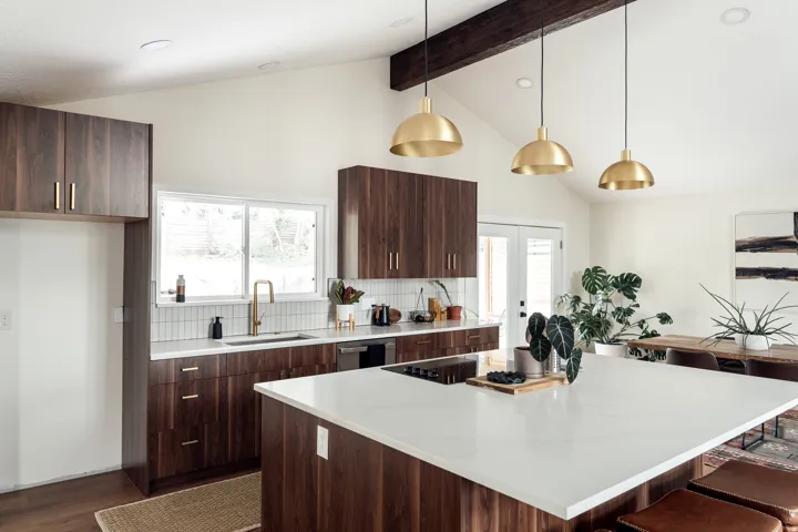Modern kitchen featuring a large central island with a white countertop, rich wood-finish cabinetry, a white subway tile backsplash, and elegant brass pendant lighting