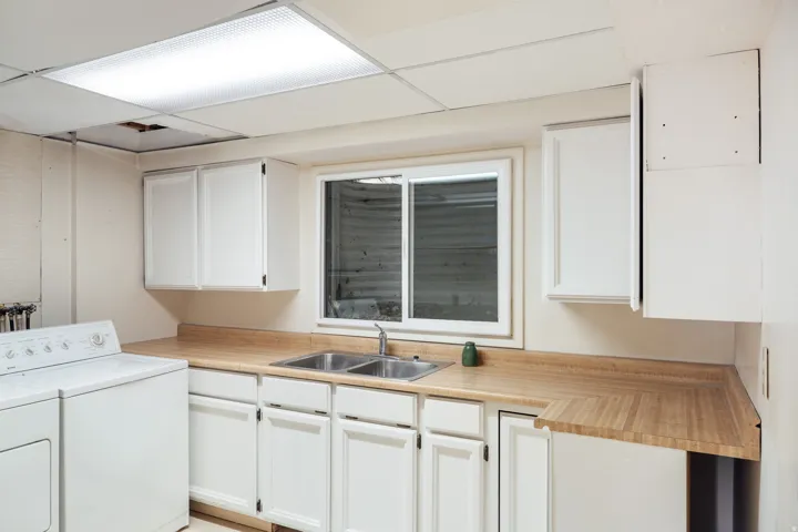 Utility space featuring white cabinetry, a double basin stainless steel sink, wood-look countertops, and a drop ceiling with integrated lighting