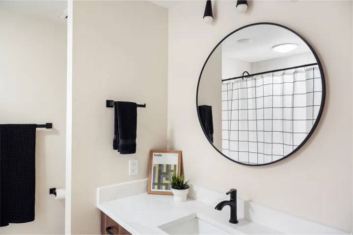 Bathroom vanity with a white countertop and integrated sink, featuring a matte black faucet and a large circular mirror