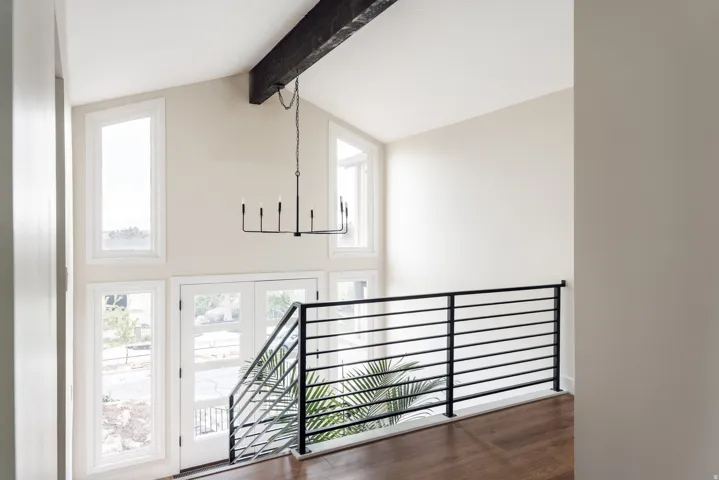 Vaulted ceiling foyer featuring a prominent exposed beam, a contemporary linear chandelier, multiple windows, double French doors, and a sleek black metal railing