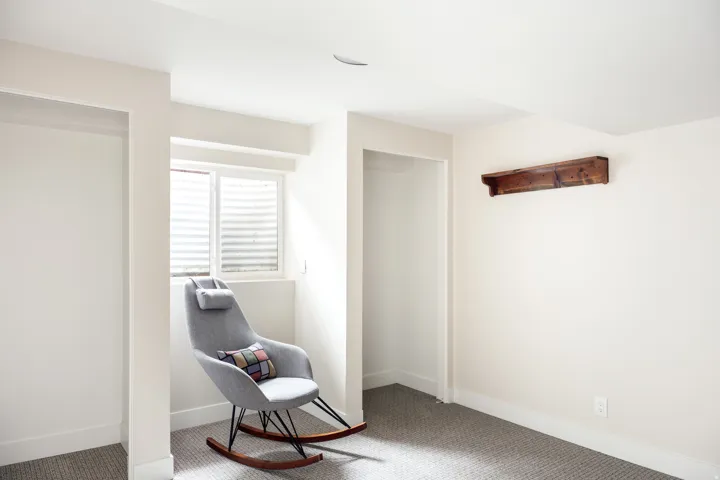 Neutral-toned room featuring a window with horizontal blinds, a decorative wood wall shelf, and two open alcoves