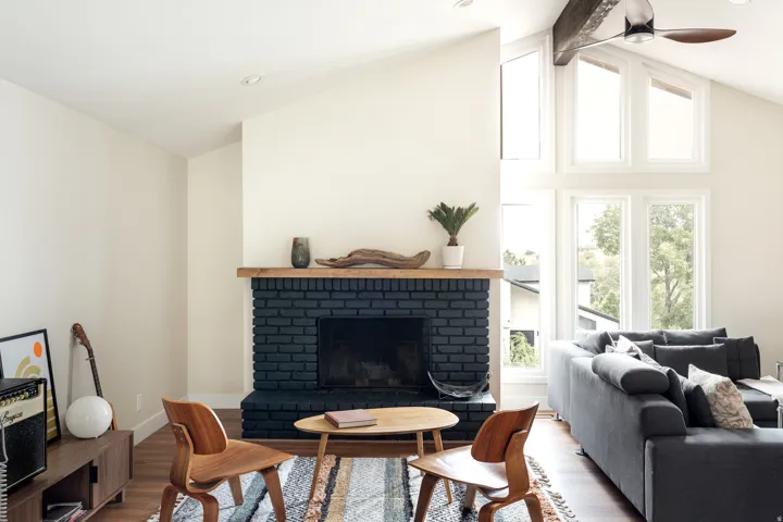Vaulted ceiling living area featuring a black brick fireplace with a wood mantle, wood-finish flooring, and a ceiling fan with integrated lighting