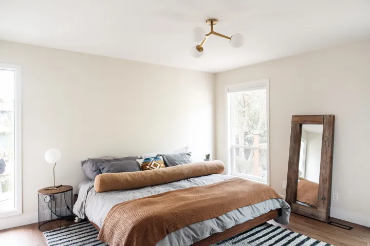 Bright room featuring two large windows, wood-finish flooring, a modern brass-finish chandelier with globe lights, and light neutral walls