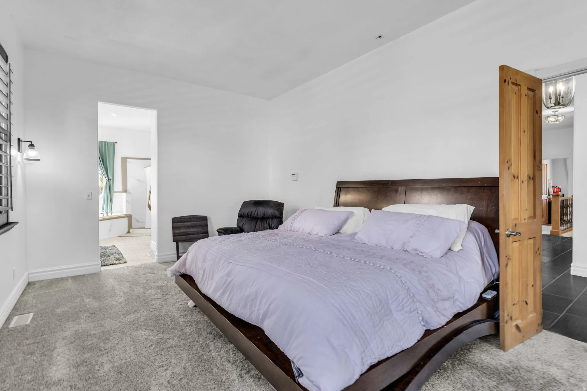 Spacious bedroom featuring plush gray carpeting, white walls, and a natural wood door