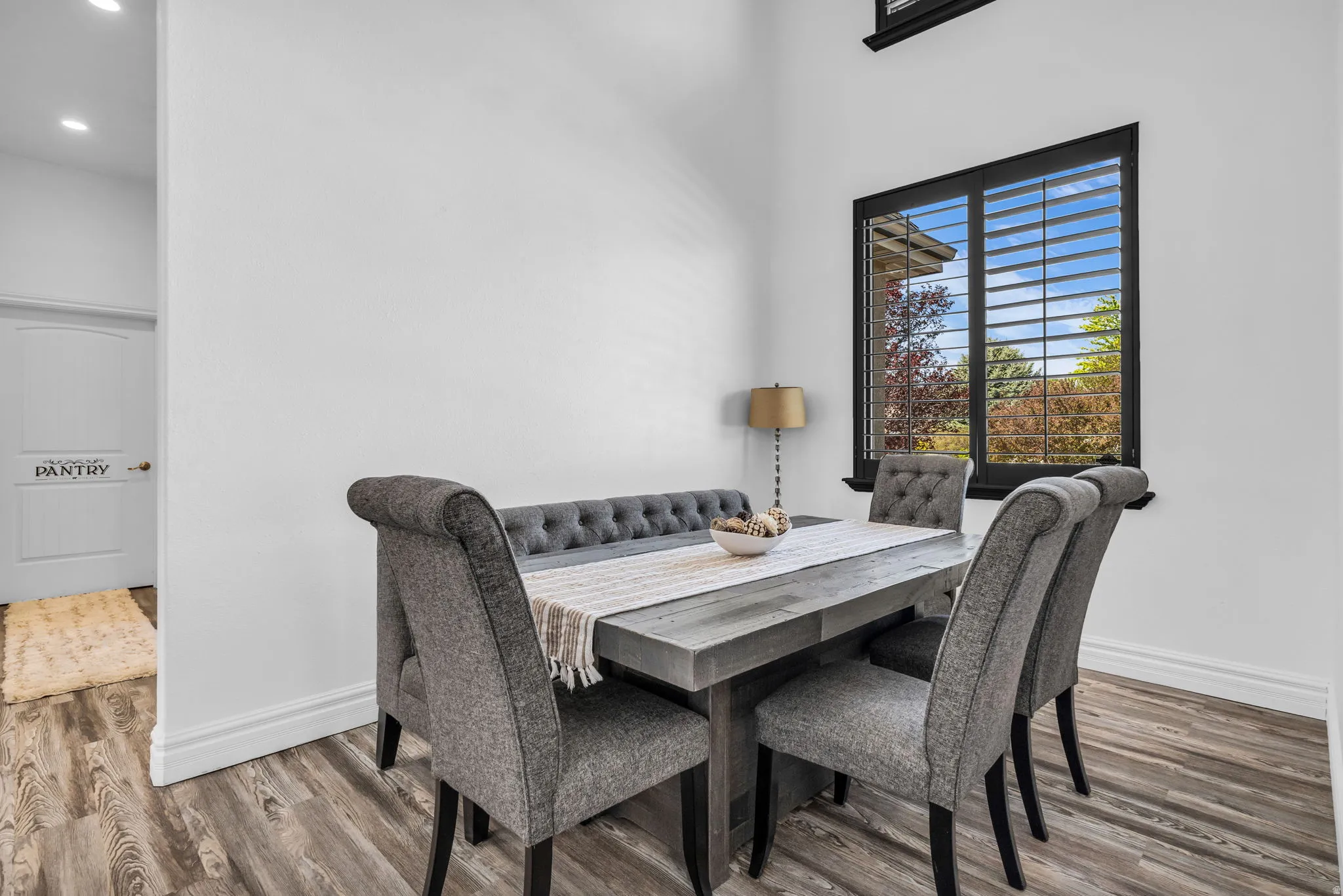 Dining area featuring wood-finish flooring, white baseboards, and a black-framed window with louvered shutters