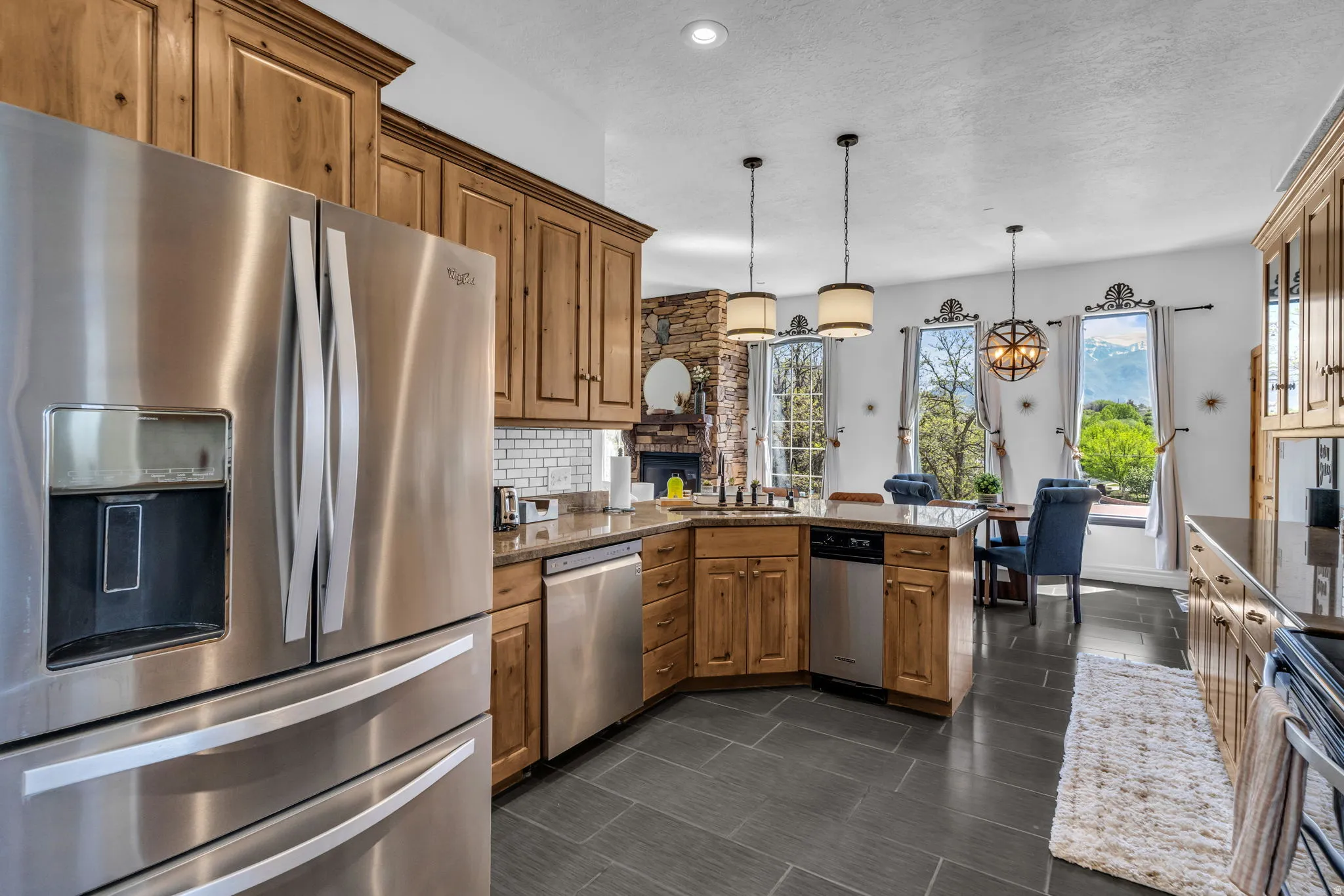 Kitchen featuring stainless steel appliances, wood cabinetry, stone countertops, and dark tile flooring