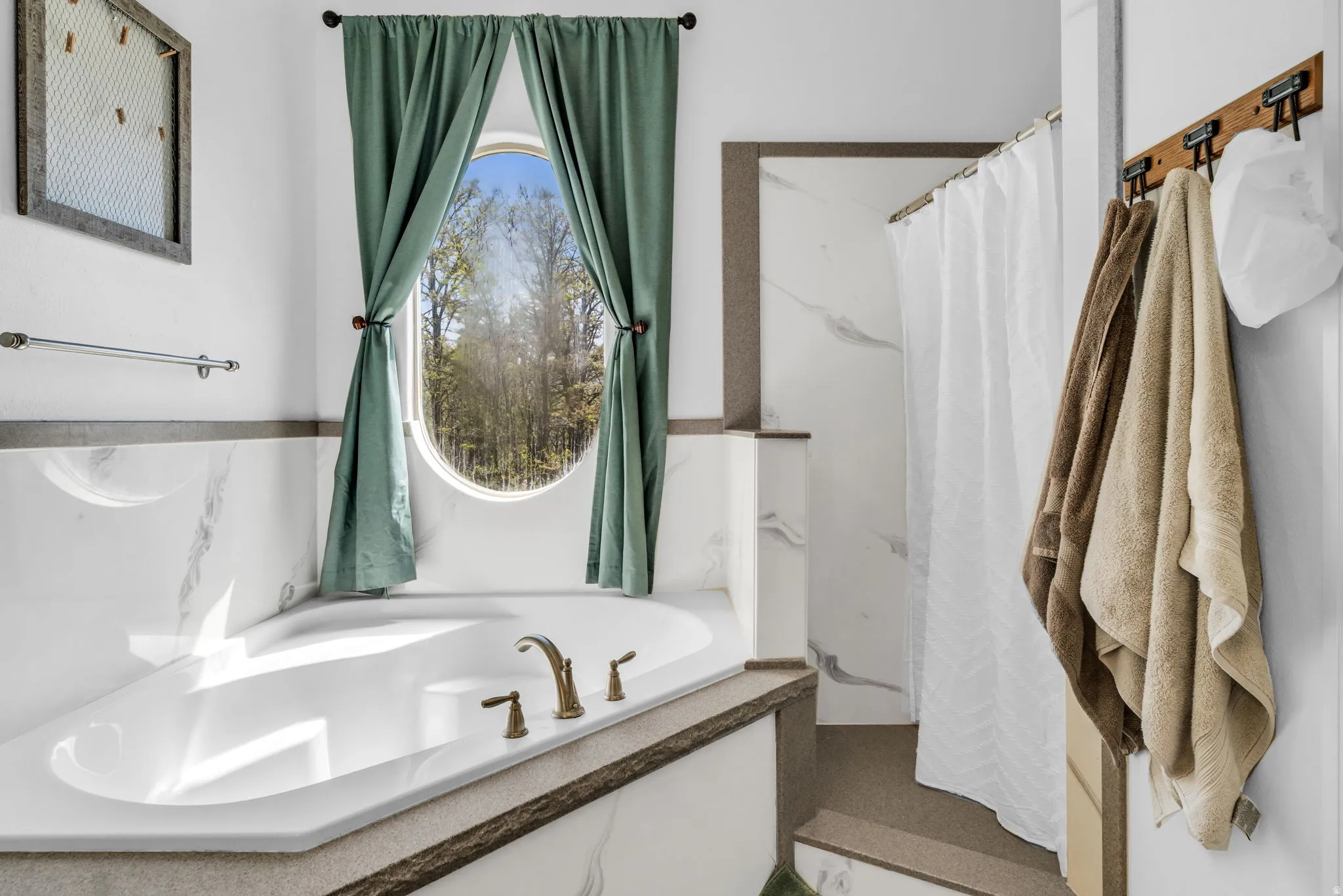 Corner soaking tub with bronze-finish fixtures, surrounded by marble-style wall paneling and a dark-toned cap