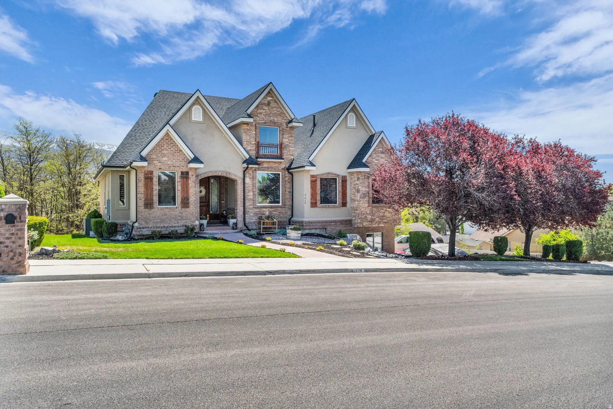 Stately two-story residence featuring a brick and stucco exterior, arched entry, multiple gables, and dark framed windows with decorative shutters
