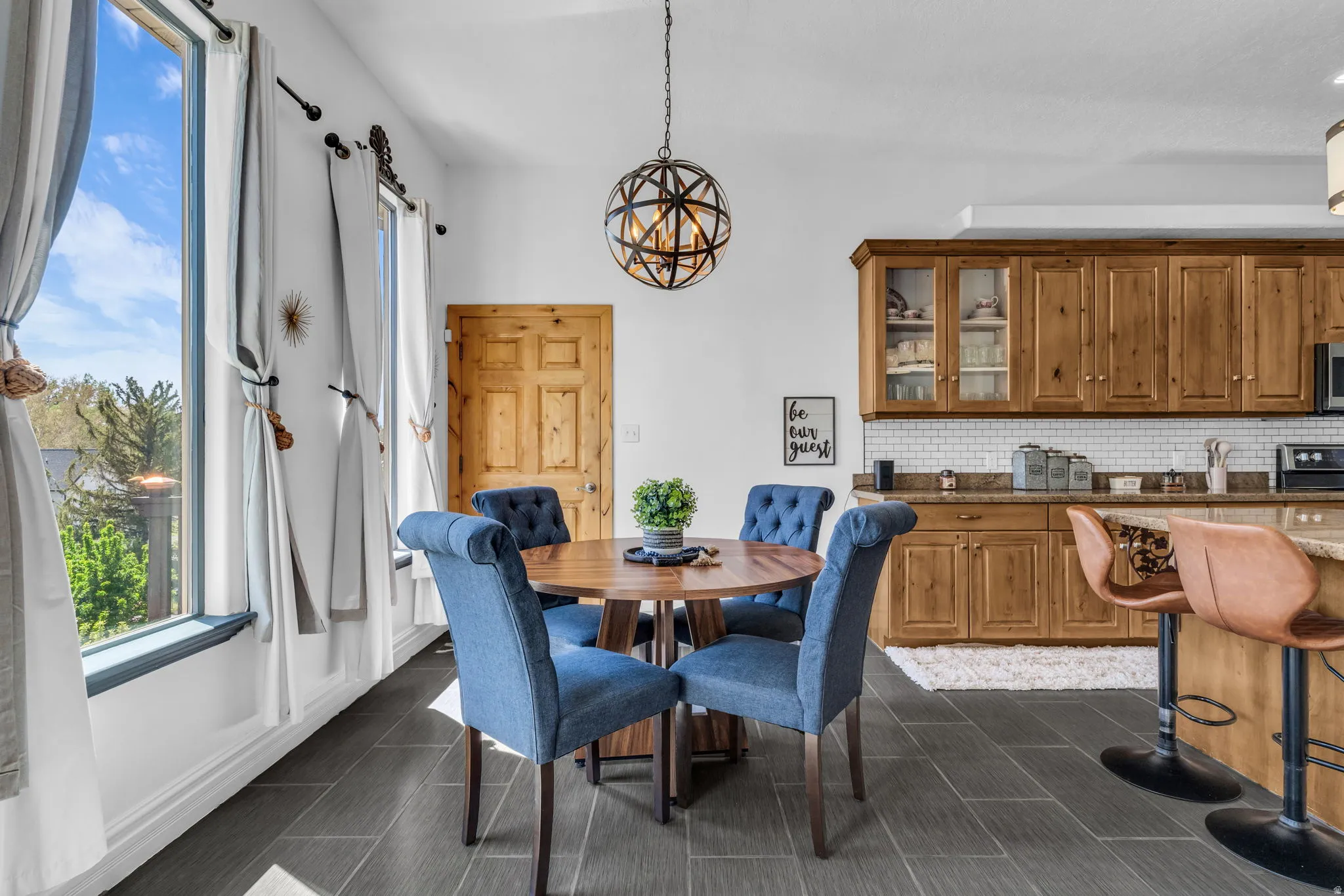 Open-concept space featuring large windows, a spherical pendant light fixture, wood-finish cabinetry, a subway tile backsplash, and stone countertops