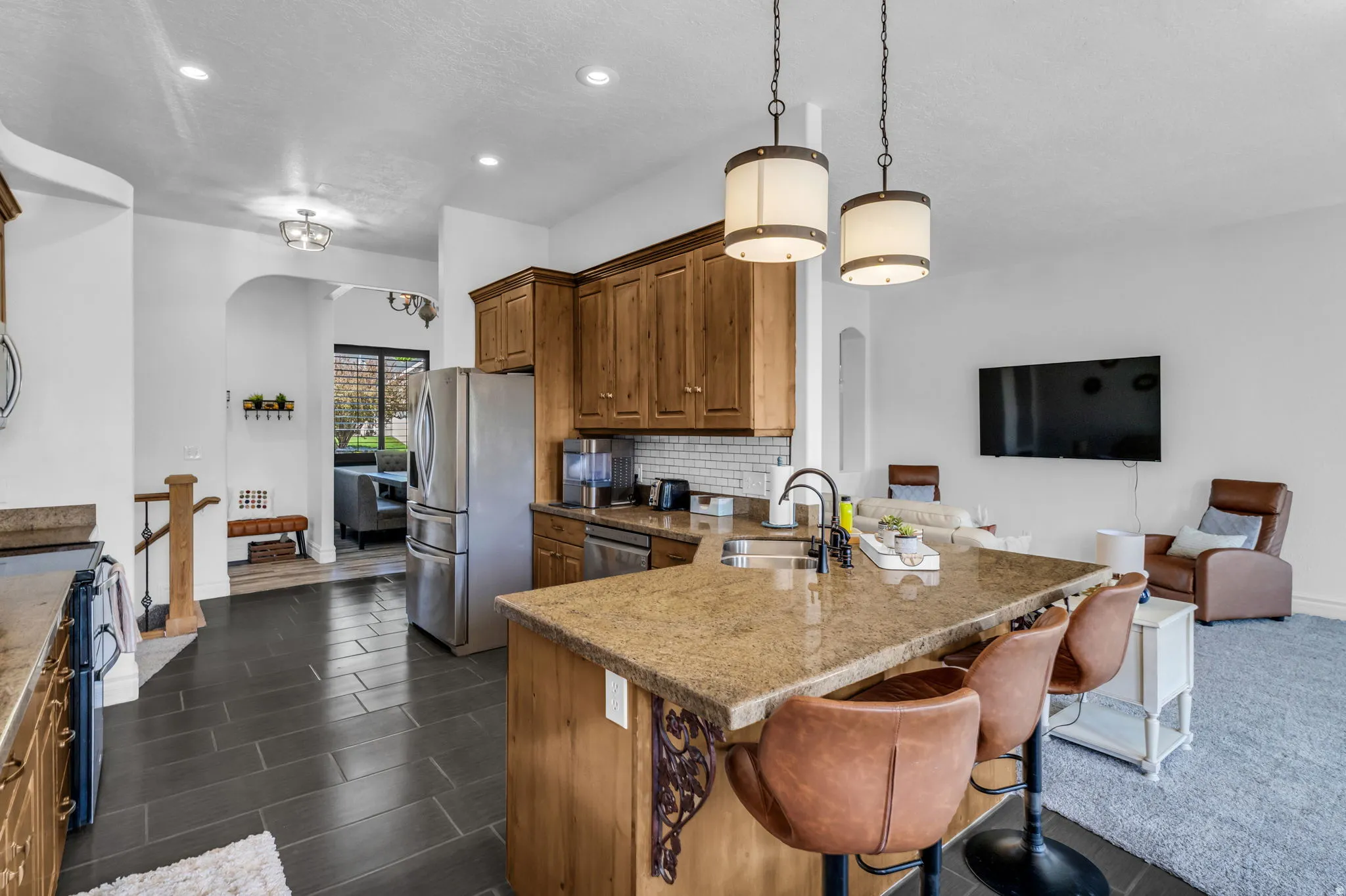 Kitchen featuring a granite island, wood cabinetry, stainless steel refrigerator, white subway tile backsplash, and black tile flooring