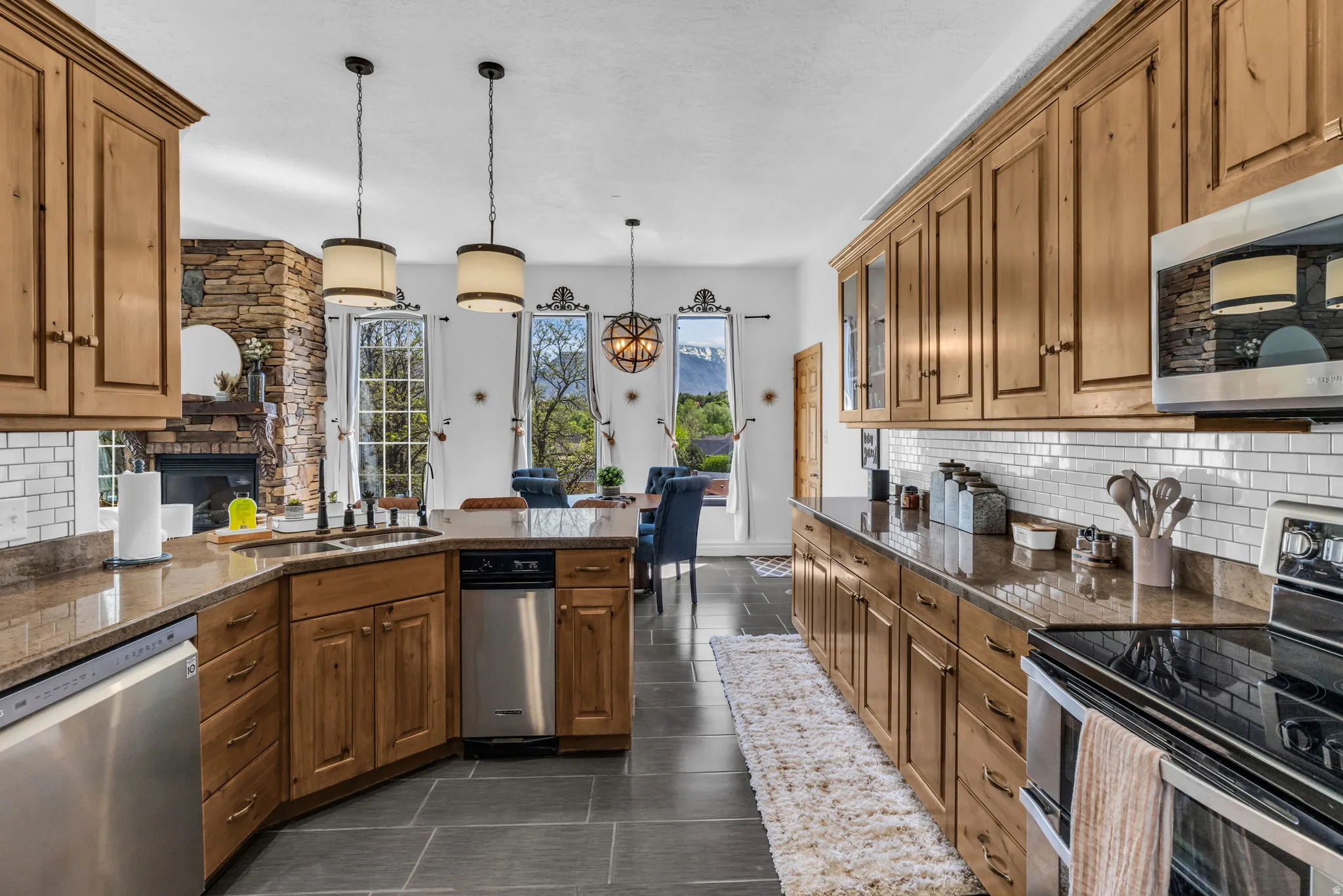 Open-concept kitchen featuring extensive wood cabinetry, granite countertops, stainless steel appliances, a white subway tile backsplash, and dark slate flooring