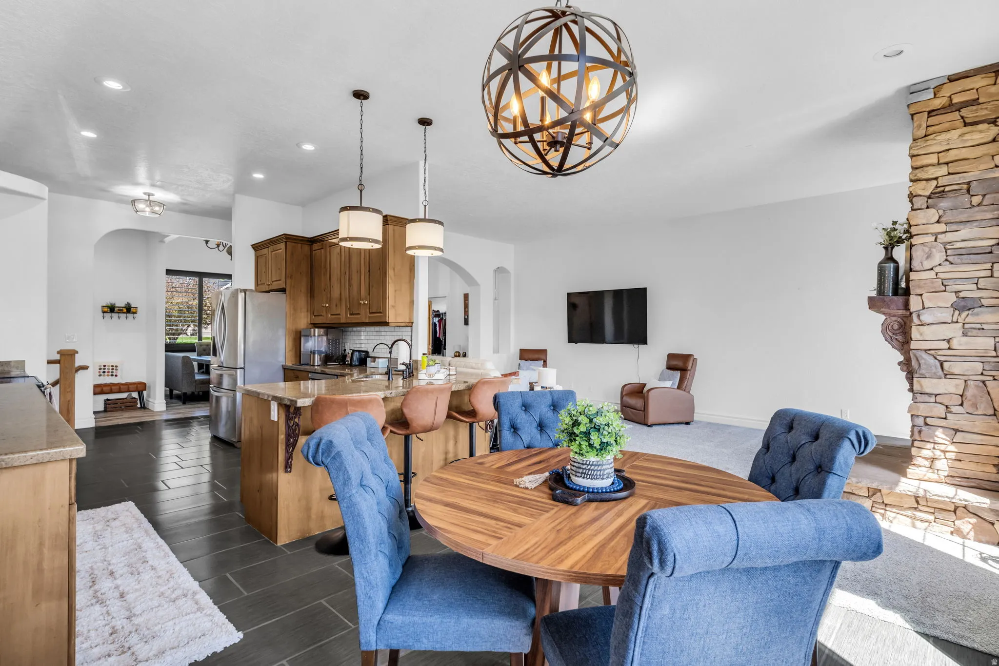 Open-concept living area featuring a stone accent wall, spherical chandelier, and dark tile flooring in the kitchen